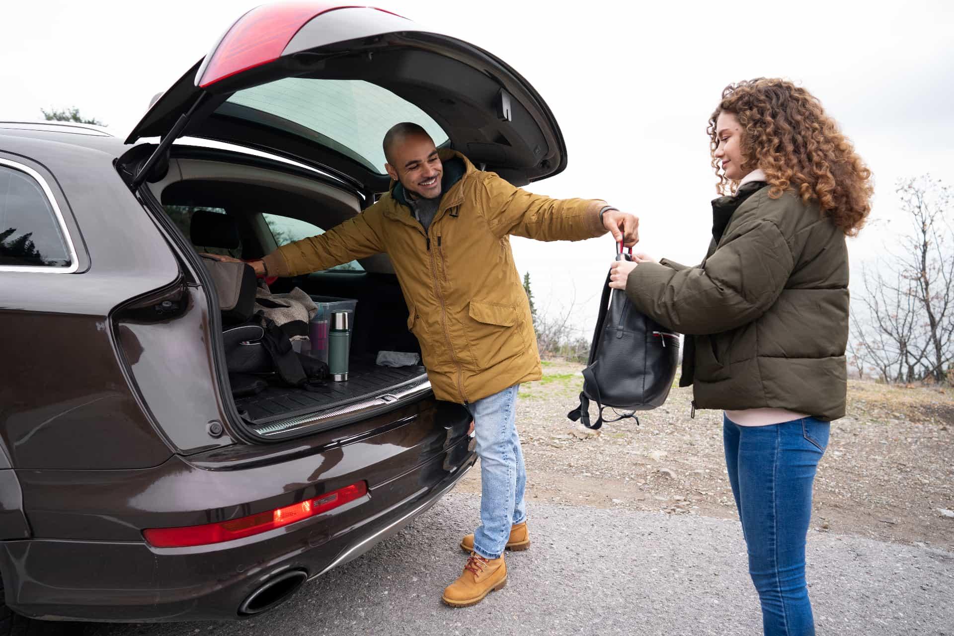 Driver helping passenger with backpack at car